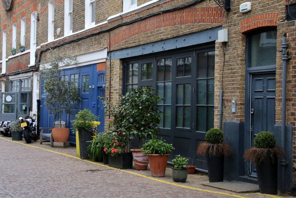 A row of traditional brick and stucco residential buildings along Finchley Road NW3, featuring well-maintained gardens with neatly trimmed hedges and flowering trees in bloom. The gardens are enclosed